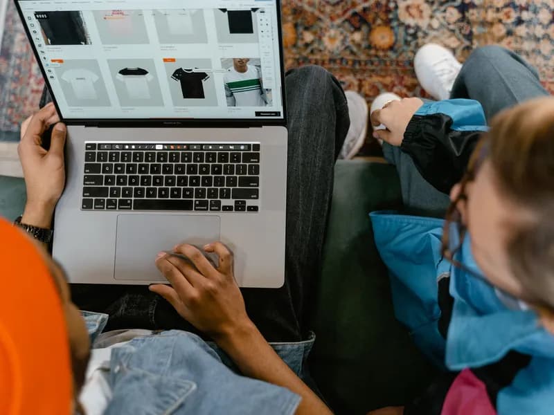 Dvoje ljudi zajedno pregledava internetsku trgovinu odjećom na prijenosnom računalu dok sjede na kauču.